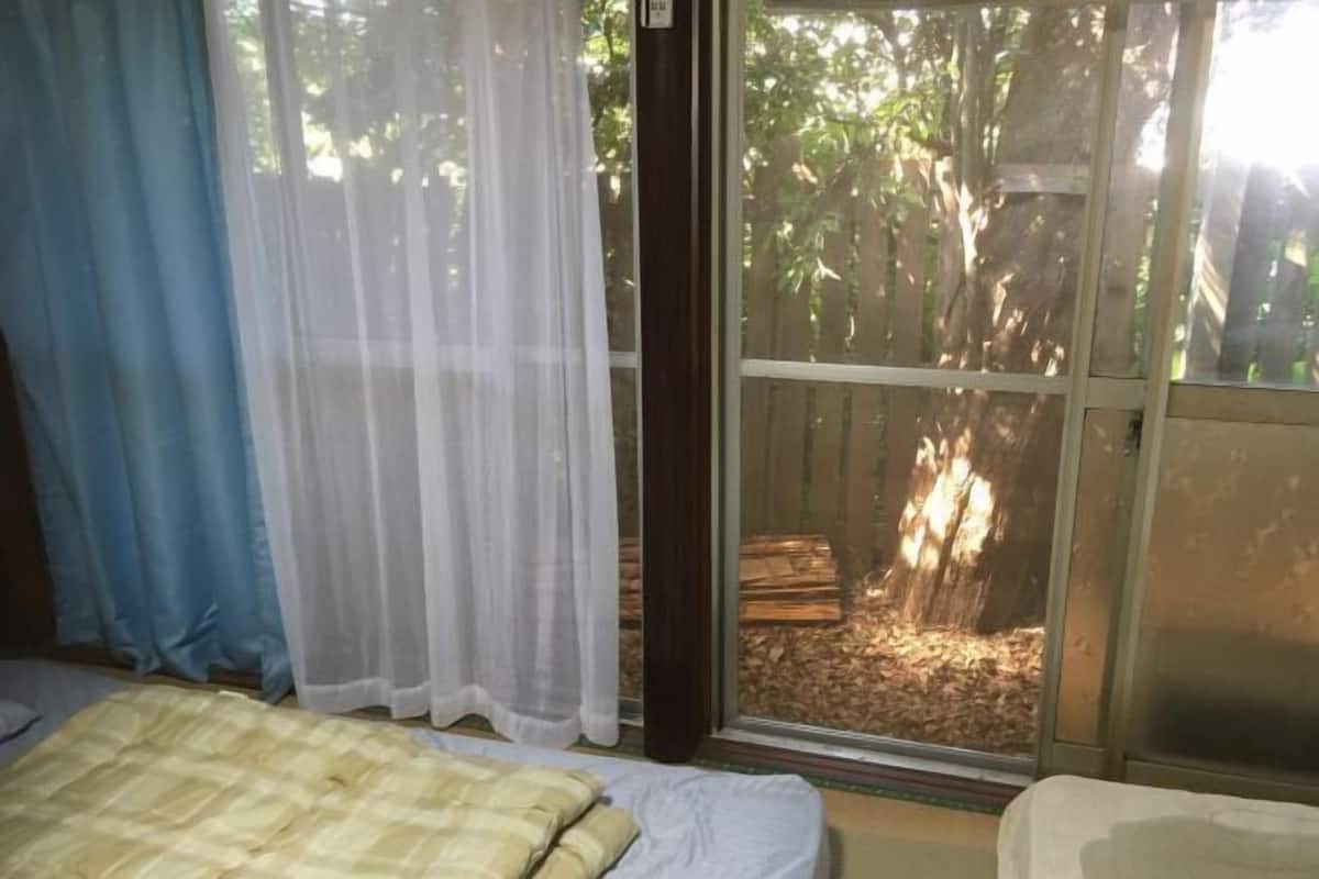 Ein Zimmer mit einem Bett und einem Fenster mit Blick auf einen Baum und Holzscheite draußen.