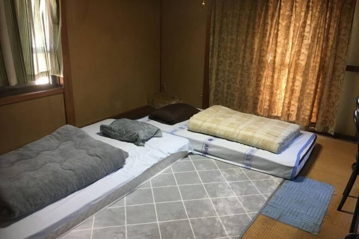 Ein Zimmer mit einem Bett, einem kleinen Tisch und einem Fenster mit Vorhängen.