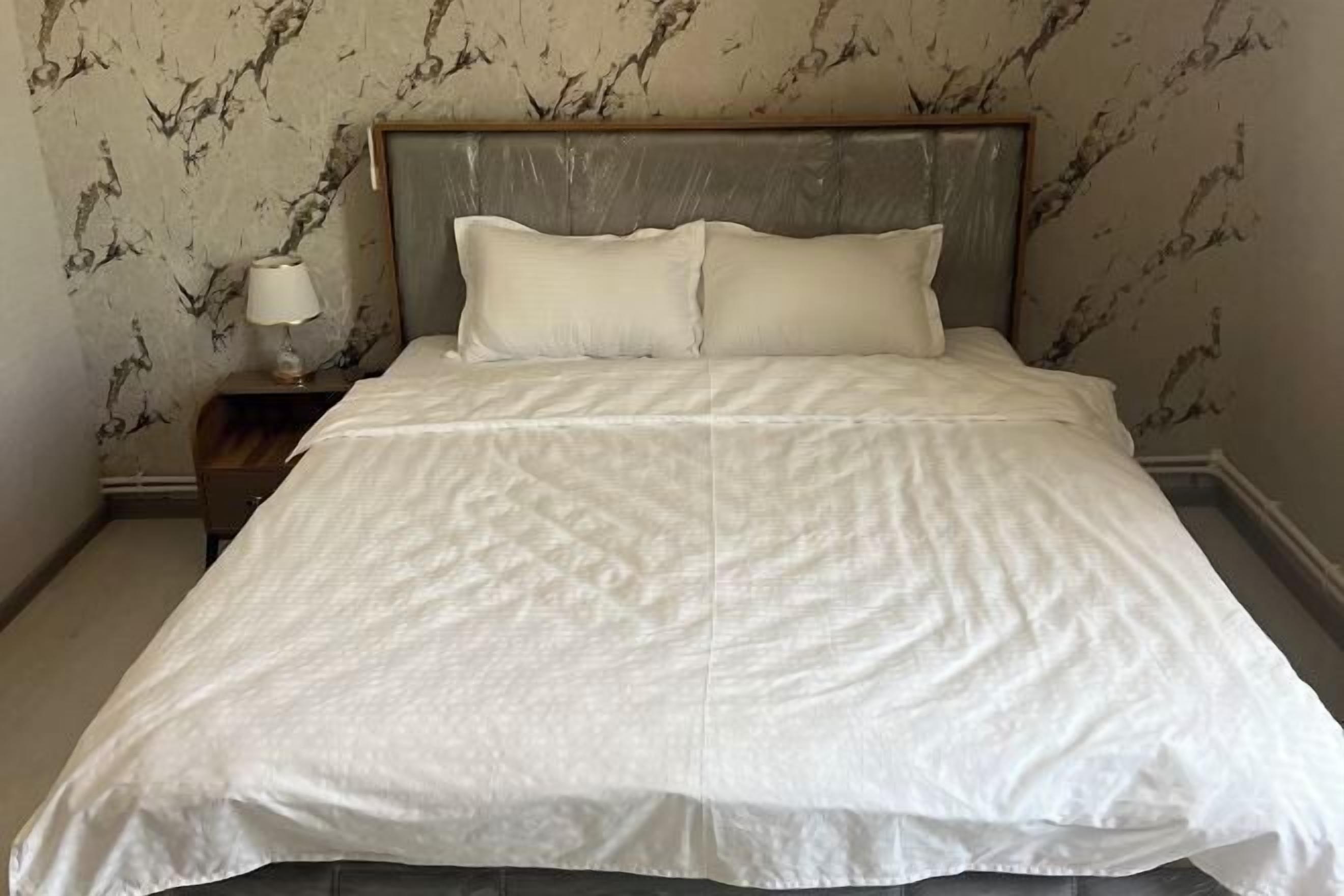 A bed with a headboard, a nightstand with a lamp, and a wall with a marble-like pattern.