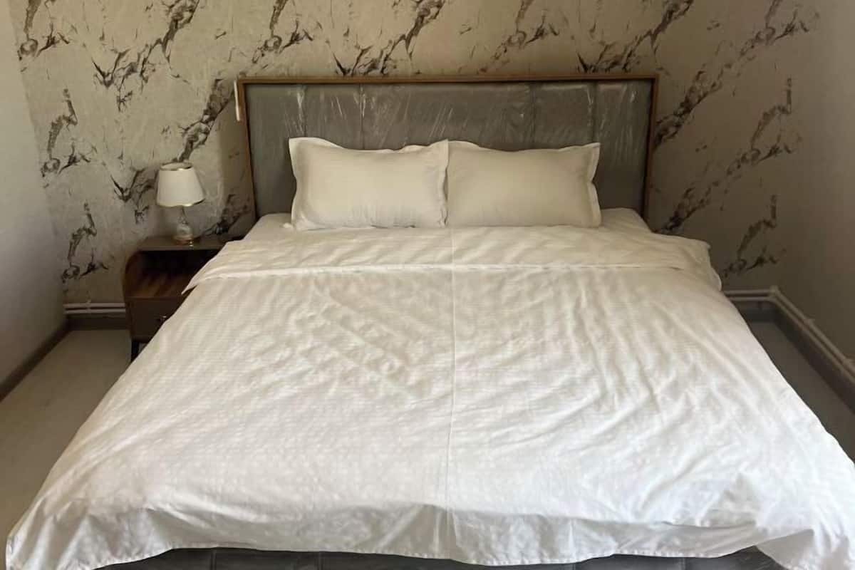 Een bed met hoofdeinde, een nachtkastje met lamp en een muur met een marmerachtig patroon.