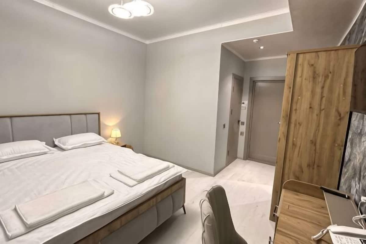 Een moderne slaapkamer met een groot bed, nachtkastjes, een houten garderobe en een bureau met een computer.