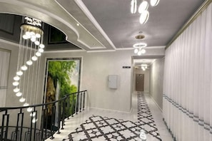 A hallway with a patterned floor, a chandelier, and a staircase. - MEHRON (Jizzakh District)
