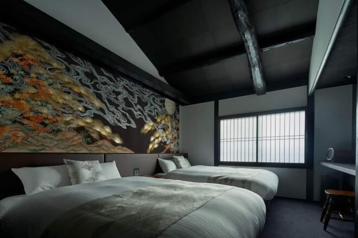Une chambre moderne avec un grand lit, une tête de lit agrémentée d’un élément décoratif mural et une fenêtre avec des stores.