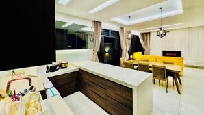 Een moderne keuken met een centraal eiland, een eethoek met een gele bank en tafel, en een trap naar een hoger niveau.
