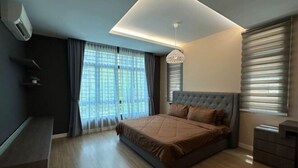 Een moderne slaapkamer met een groot bed, een inbouwsbankje, een plafondlamp en een raam met jaloezieën.