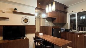 A modern kitchen with wooden cabinets, a built-in TV, a dining table with chairs, and pendant lights. - Sweet Home (2 Bedroom Apartment) (Mulyorejo)
