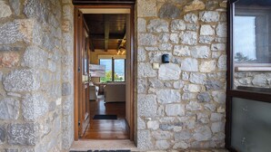 Un interno con pareti in pietra che conduce a una stanza con soffitto in legno e vista sull'esterno.