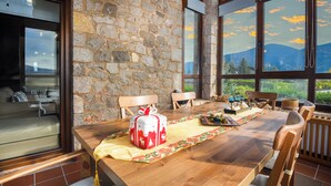 Un tavolo da pranzo in legno con un centro tavola festoso, pareti in pietra e ampie finestre con vista sulle montagne.