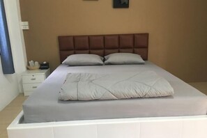 En pænt redt seng med knægt, et natbord med lampe, og en vægmonteret lyskontakt.