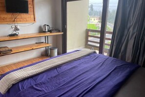 A bedroom with a bed, wooden shelves, a television, and a balcony with a view. - Homestay Semesta Bromo (Sukapura)