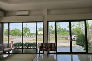 A spacious room with large windows, a seating area, and a view of a road and greenery. - The White Residence (Chanthaburi)