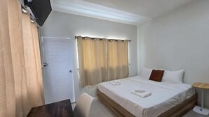 A hotel room with a bed, a desk, a chair, a TV, and a door. - The White Residence (Chanthaburi)