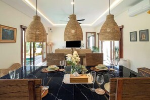 A dining area with a black marble table, wicker chairs, and hanging light fixtures. - Villa Lange 2 (Bali)