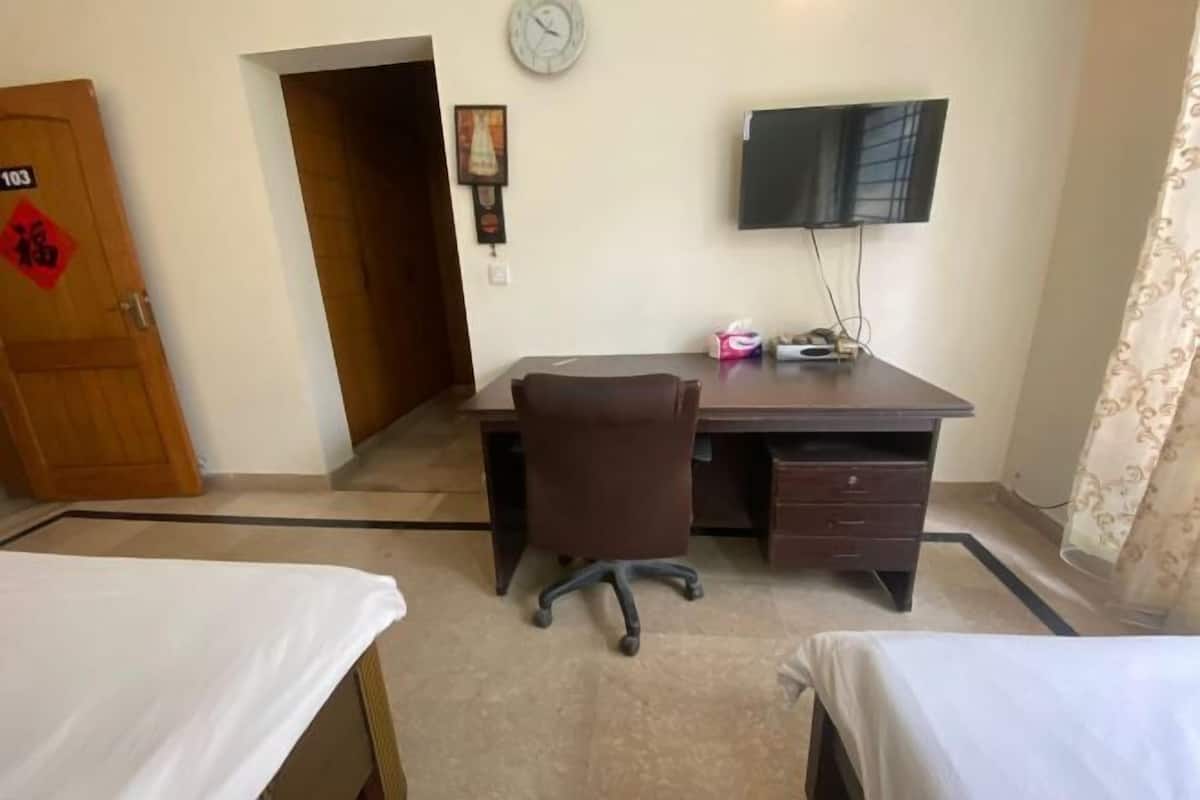 A room with a desk, two beds, a TV, and a clock on the wall.