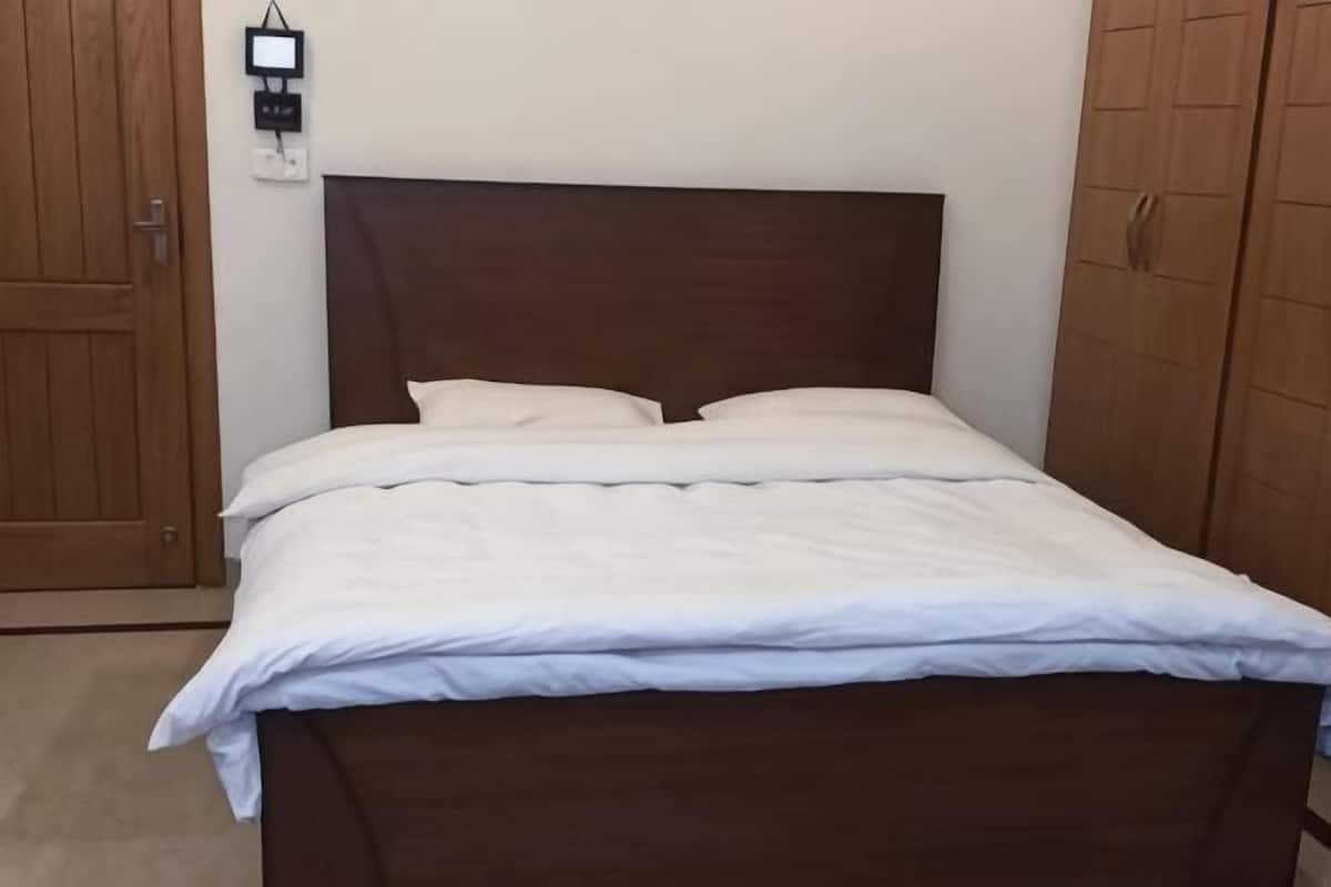 A bed with a wooden headboard, white bedding, and a power outlet on the wall.
