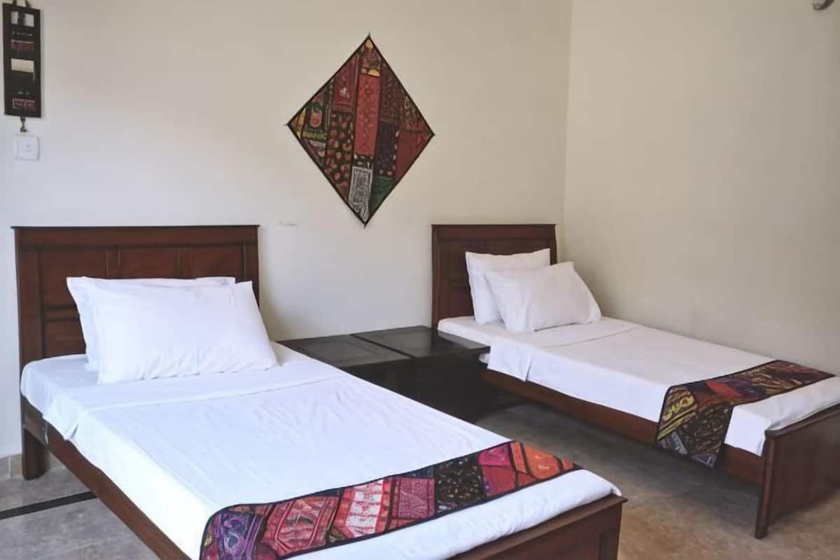 Two single beds with wooden headboards, a small table, and a decorative wall hanging.