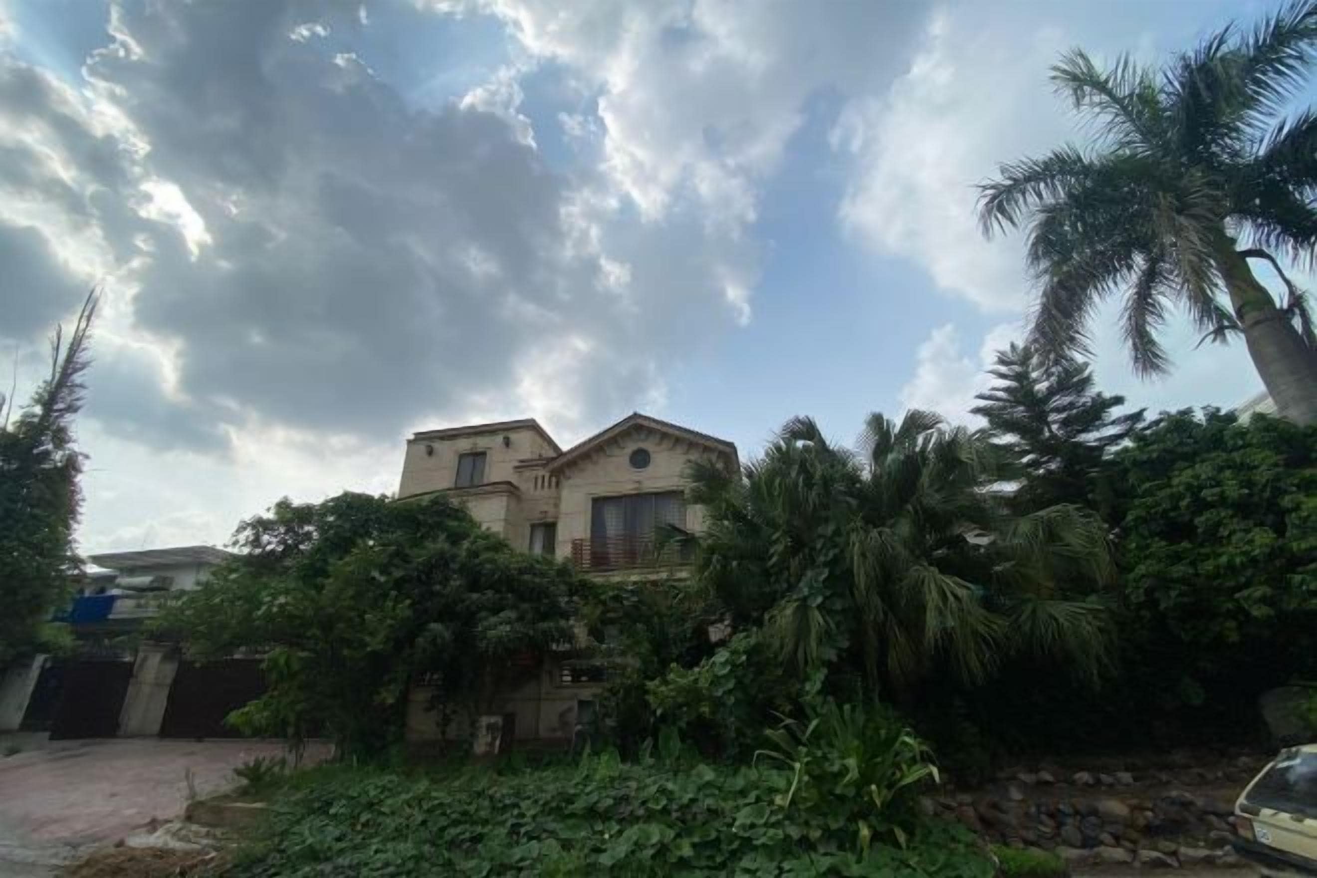 Ein zweistöckiges Gebäude mit Balkon, umgeben von üppiger Vegetation und einer Palme.