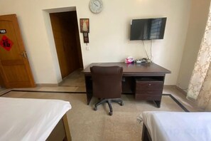 A hotel room with a bed, a desk with a chair, a television, and a clock on the wall. - Costco Chinese Hotel (Islamabad)
