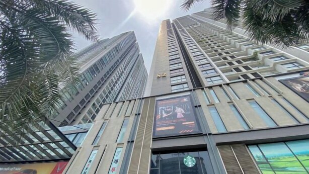 A tall building with a Starbucks sign, palm trees, and a large advertisement on the side. - Vinhomes Skylake Residence Hanoi City - Mango Housing (Hanoi)