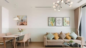 A modern living room with a sofa, coffee table, dining table, and chairs. There are three framed artworks on the wall and a pendant light above the sofa. - Vinhomes Skylake Residence Hanoi City - Mango Housing (Hanoi)