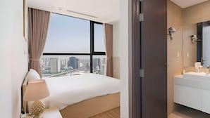 A modern hotel room with a large bed, a view of the cityscape, a bathroom with a large mirror, and a nightstand with a lamp. - Vinhomes Skylake Residence Hanoi City - Mango Housing (Hanoi)