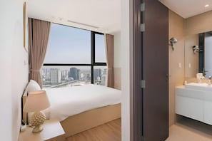 A hotel room with a large bed, a nightstand, a lamp, a bathroom with a sink and mirror, and a city view. - Vinhomes Skylake Residence Hanoi City - Mango Housing (Hanoi)