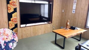 A room with a large flat-screen TV mounted on the wall, a wooden table with a laptop, and a small statue. - Injie Hotel Shimonoseki (Shimonoseki)