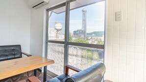 A room with a large window, a wooden table, a leather sofa, and a wall-mounted air conditioner. - Injie Hotel Shimonoseki (Shimonoseki)