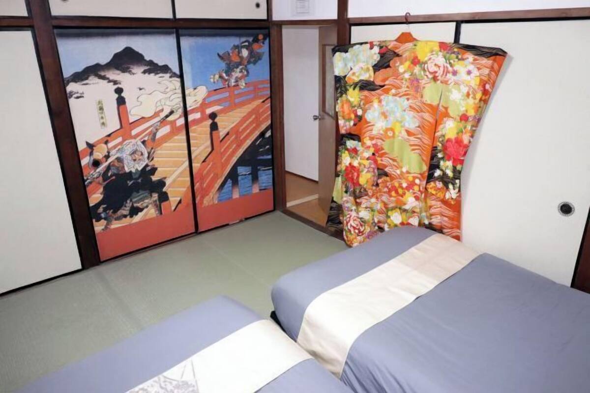 A room with two beds, a traditional Japanese sliding door with artwork, and a colorful kimono hanging on the door.