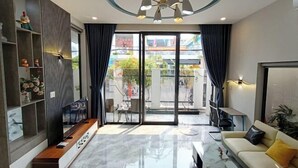 A modern living room with a sofa, coffee table, and a built-in TV unit. There is a sliding glass door leading to an outdoor balcony. - Aroma Beach (Da Nang)
