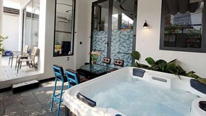 A modern outdoor hot tub area with a glass partition, a dining table with chairs, and a view of the outside. - Aroma Beach (Da Nang)