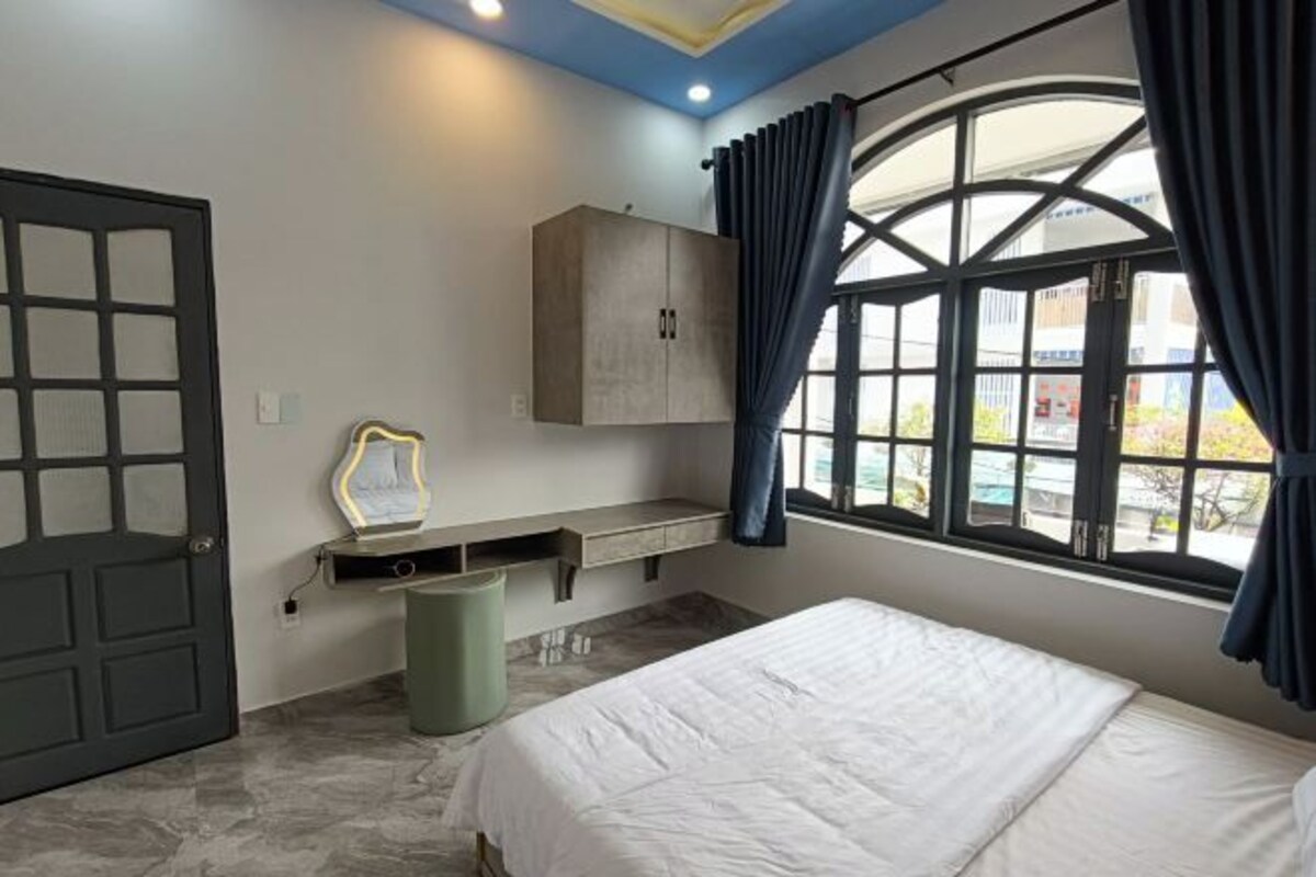 A bedroom with a bed, a wardrobe, a desk with a mirror, and a window with curtains.