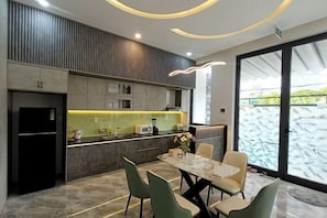 A modern kitchen with a dining area, featuring a marble countertop, a refrigerator, and a dining table with chairs. - Aroma Beach (Da Nang)