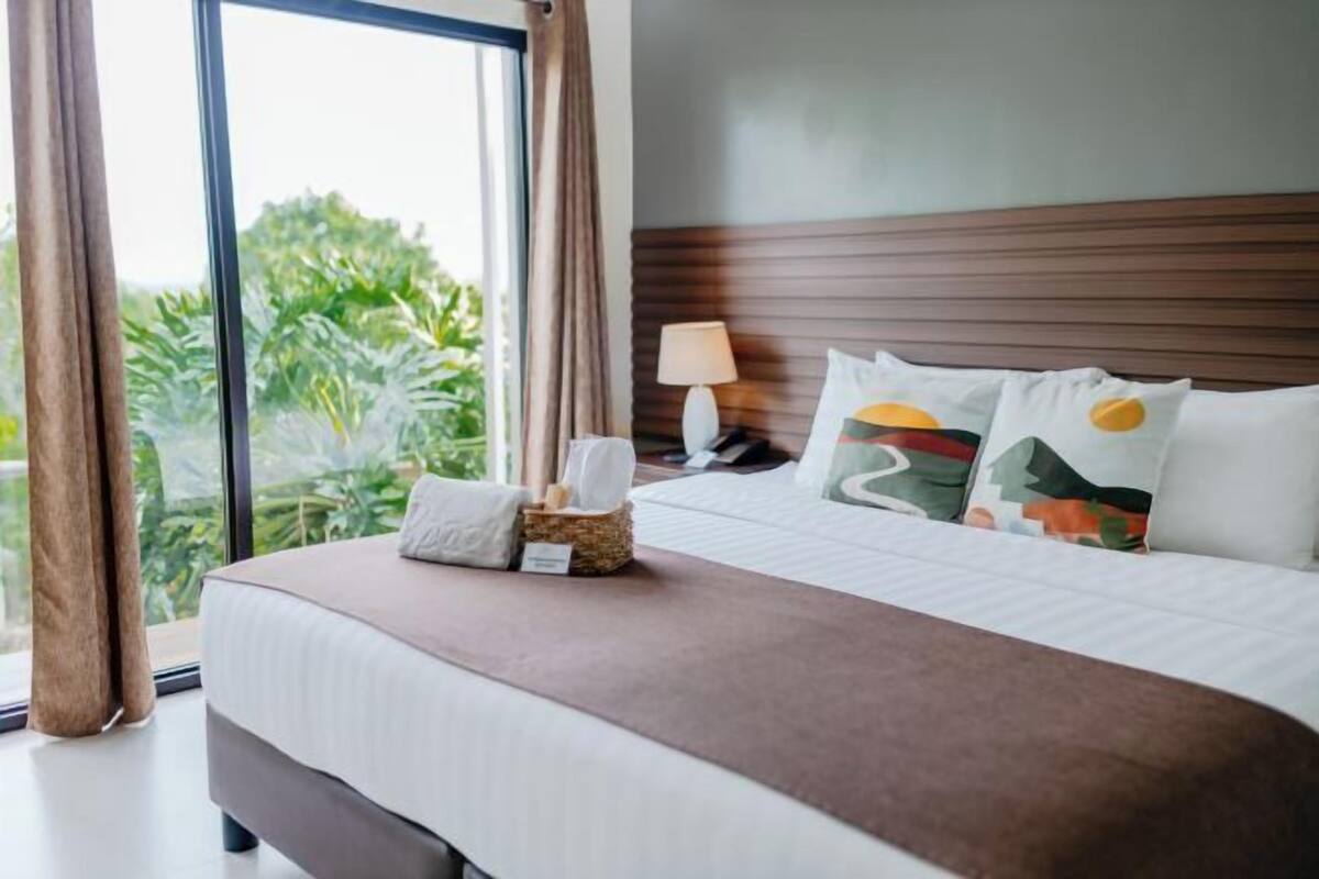 Une chambre d’hôtel avec un grand lit, une table de chevet avec une lampe et une vue sur la verdure.
