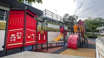 Um parquinho com diversas estruturas de recreação, incluindo uma parede de escalada vermelha, um escorrega e um tobogã vermelho.