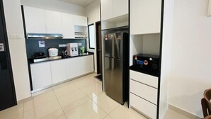 A modern kitchen with white cabinets, a stainless steel refrigerator, and a black countertop. - Desaru Utama A14 by UcomeHomestay (Bandar Penawar)