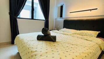 A hotel room with a bed, a window with curtains, a bedside table, and a wall-mounted light fixture.