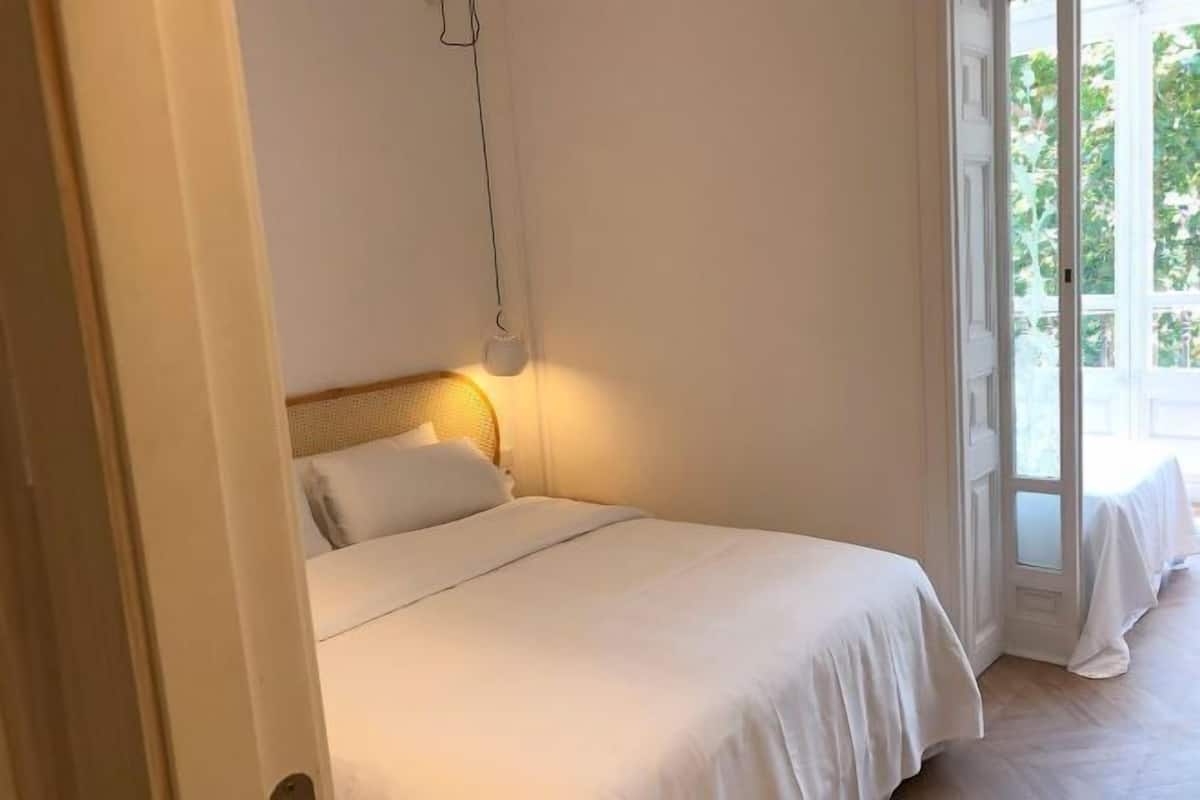 A bedroom with a bed, a hanging light fixture, and a view through a glass door.
