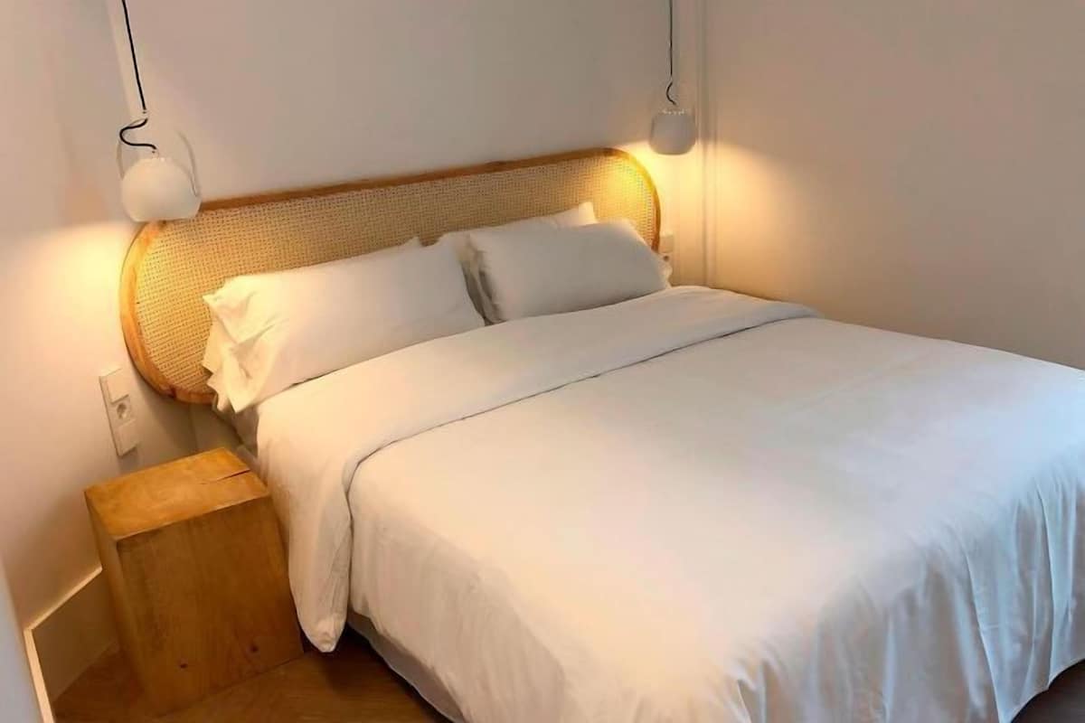 A neatly made bed with white linens, a wooden headboard, and bedside lamps.
