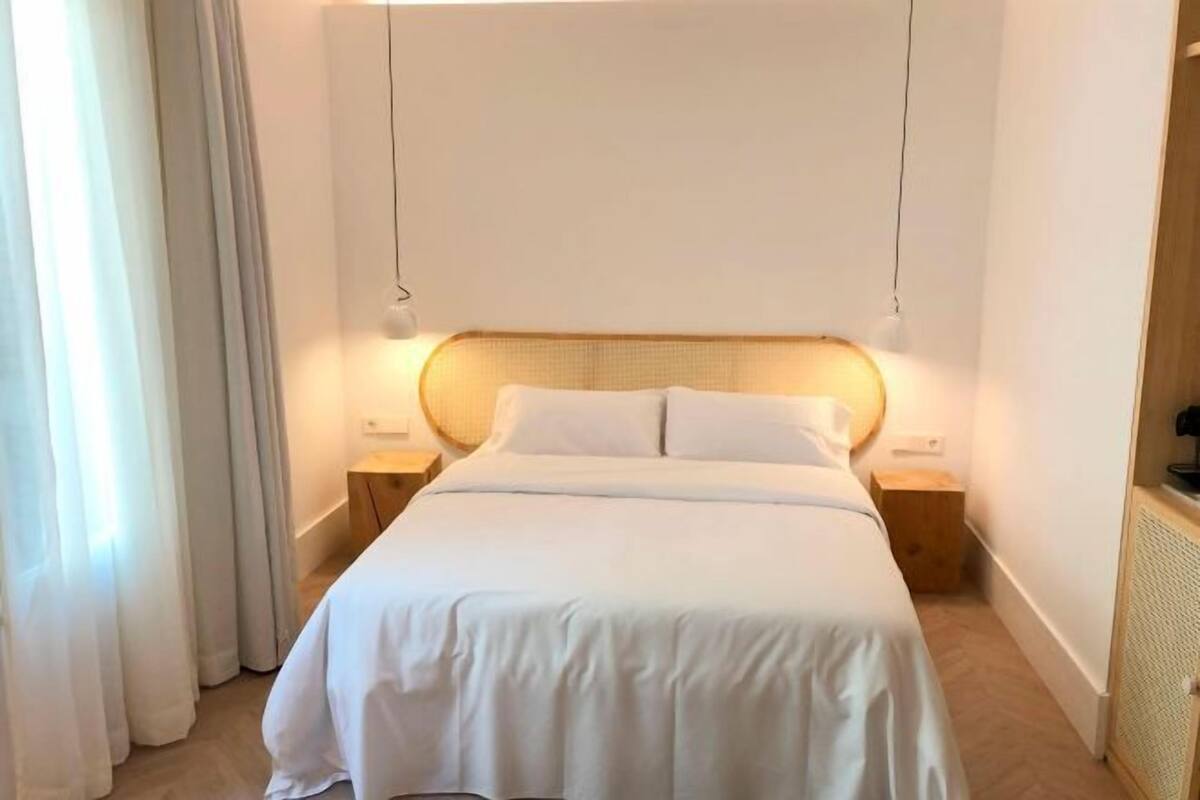 A neatly made bed with white linens, a wooden headboard, and bedside lamps.