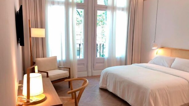 Une chambre d’hôtel avec un lit, un bureau avec une lampe, une chaise et un téléviseur fixé au mur.