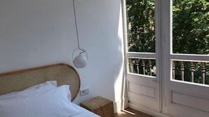 Une chambre à coucher avec un lit, une lampe de chevet, un petit tabouret en bois et une fenêtre donnant sur un paysage verdoyant.