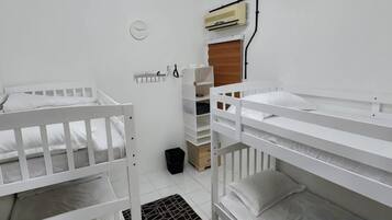 Quarto com beliches, uma pequena janela e ar condicionado fixado na parede.