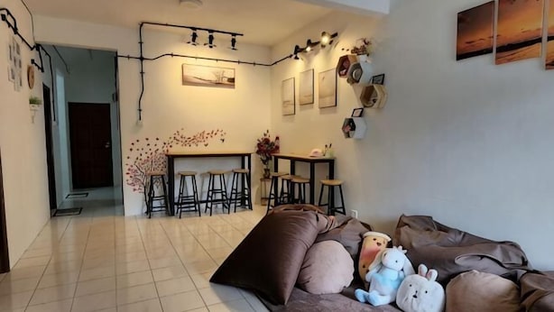Een woonkamer met een bank, een eethoek met krukken, en een keuken op de achtergrond.
