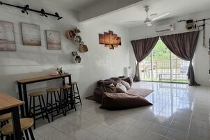 A modern living room with a sofa, a dining table with stools, a ceiling fan, and a large window with curtains.