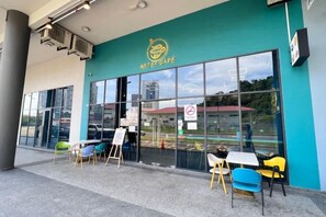 An outdoor seating area with tables and chairs in front of a building with a teal facade and large windows. - JQ Unity Homestay Seaview 6pax (Kota Kinabalu)