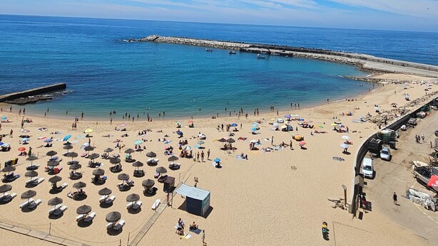 Una spiaggia con ombrelloni, lettini e un molo sullo sfondo.