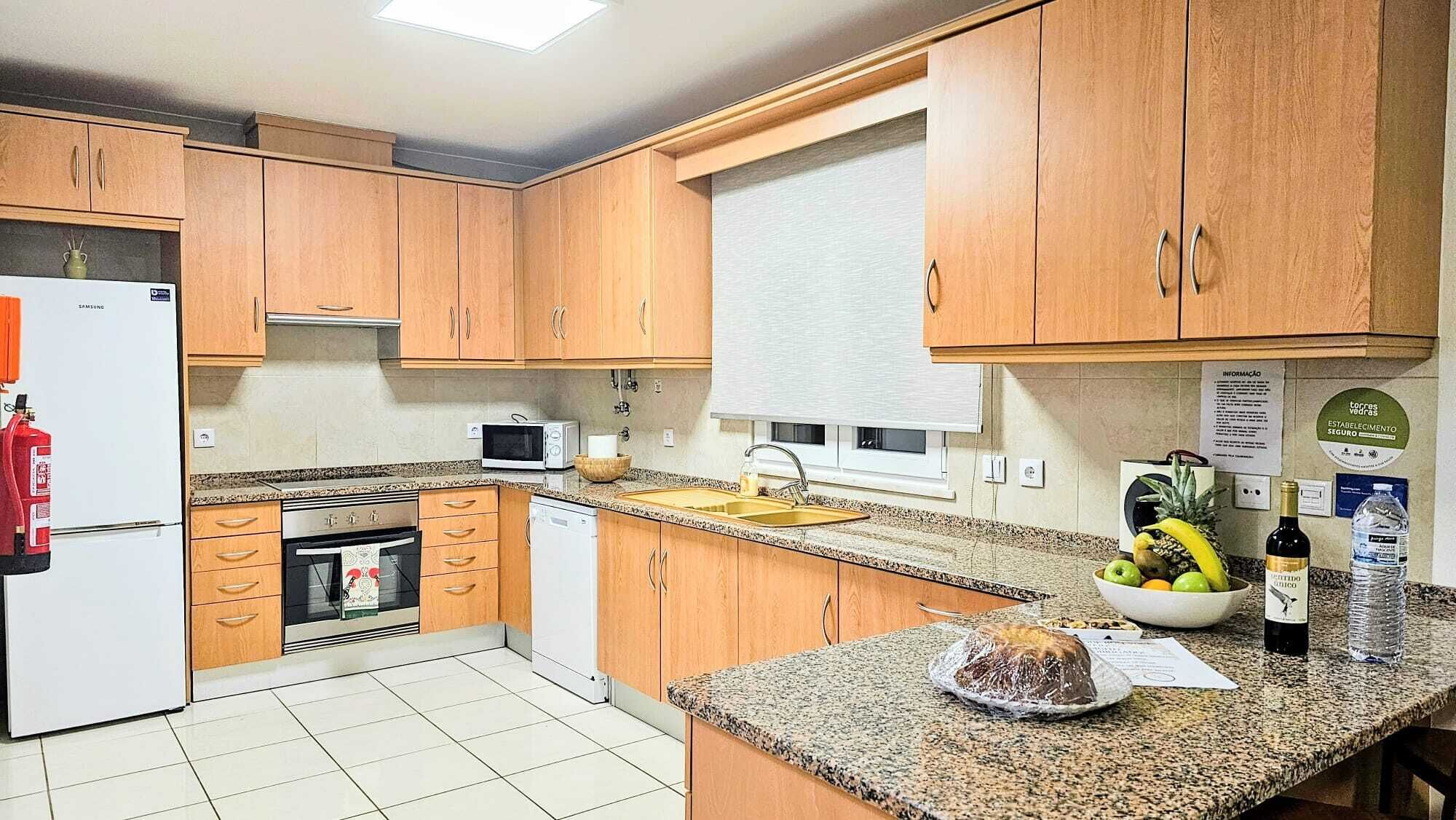A kitchen with wooden cabinets, a microwave, a sink, and a countertop with a loaf of bread, a bottle of wine, and a water bottle.