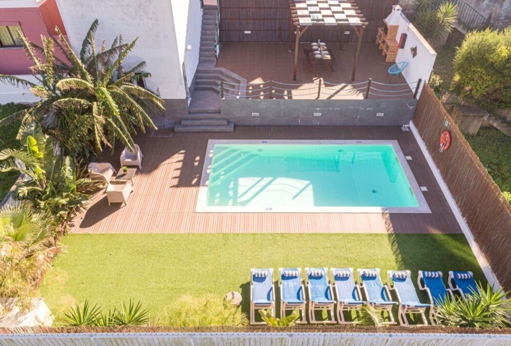 A rectangular swimming pool with a wooden deck, surrounded by a grassy area and a few lounge chairs.