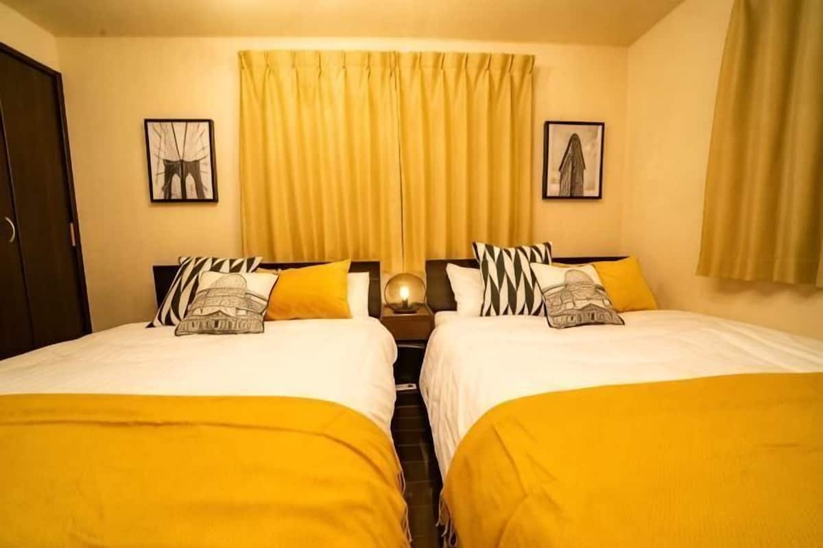 A hotel room with two beds, a nightstand, and a large window with curtains.